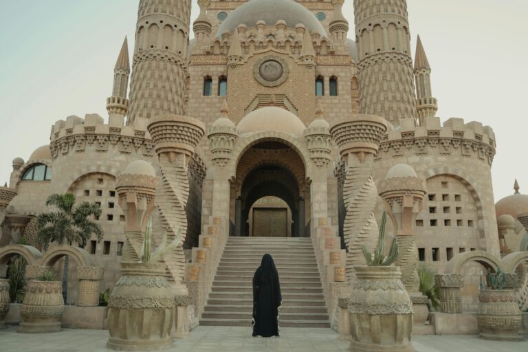 A woman in black robe stands before an intricate mosque, highlighting traditional architecture.